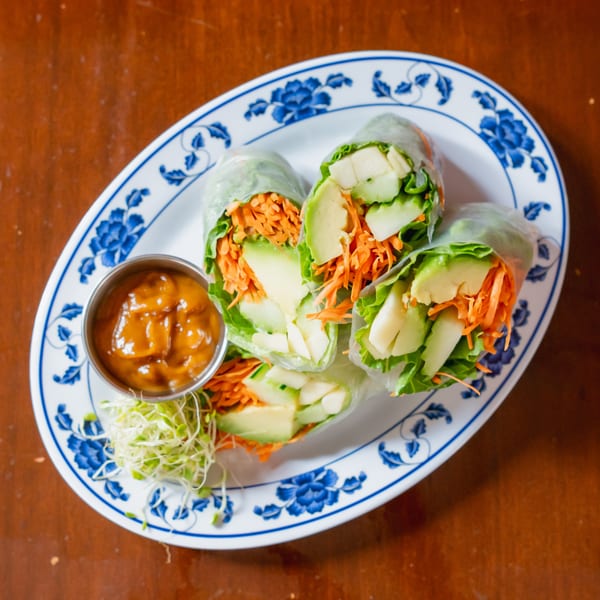 Fresh spring rolls filled with avocado, carrots, and lettuce, served with peanut sauce and sprouts.