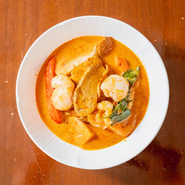 Overhead view of a white bowl filled with red curry, shrimp, scallops, and vegetables.