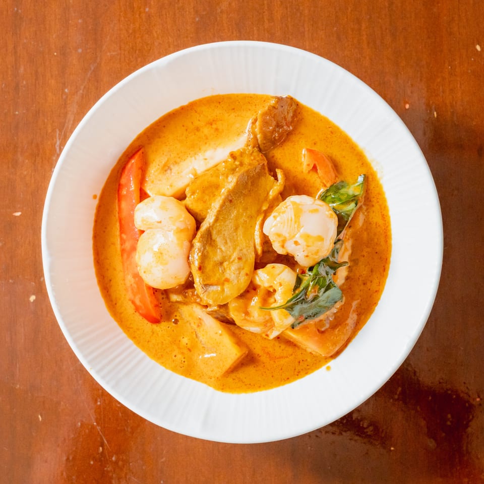 Overhead view of a white bowl filled with red curry, shrimp, scallops, and vegetables.