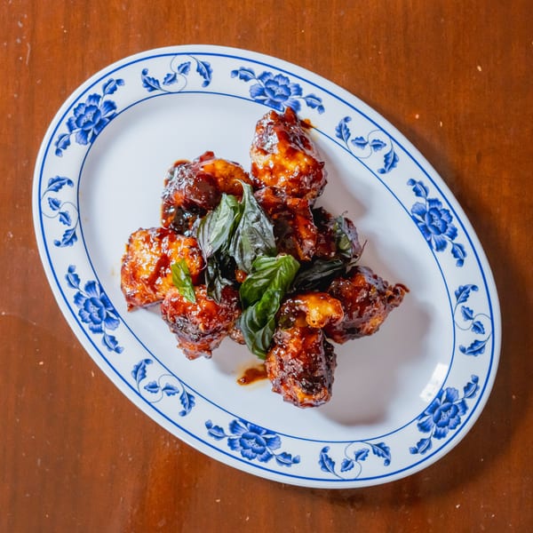 Sweet and sour chicken bites with fresh basil on a white oval plate with blue floral trim.