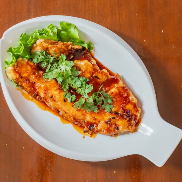 Sweet and sour fish fillet with cilantro and lettuce on a white, leaf-shaped plate.