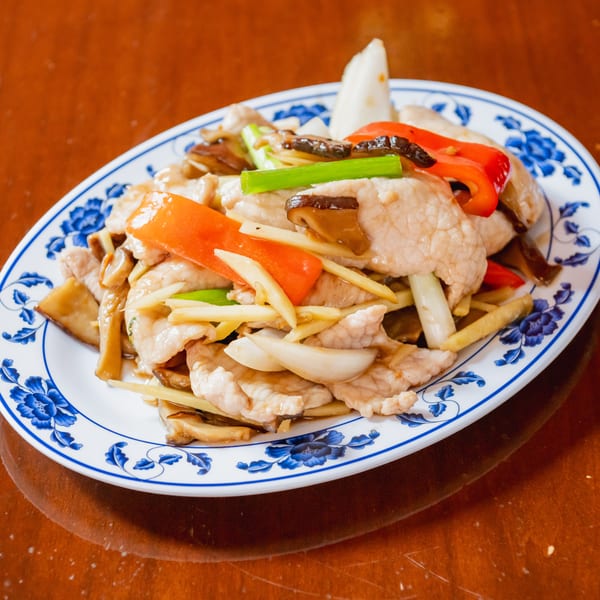 Stir-fried chicken with red peppers, onions, mushrooms, and ginger on a blue and white plate.