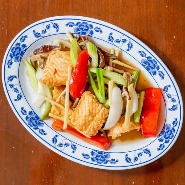 Stir-fried tofu with red peppers, celery, onions, and mushrooms on a blue and white patterned plate.