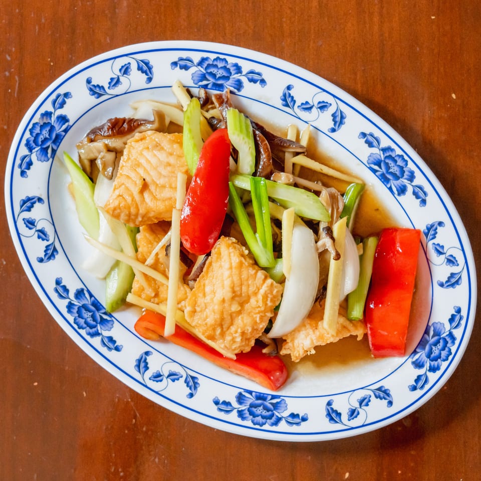 Stir-fried tofu with red peppers, celery, onions, and mushrooms on a blue and white patterned plate.