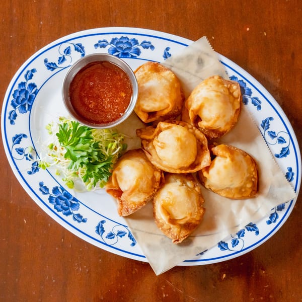 Six golden-fried wontons with a side of red dipping sauce and fresh sprouts on a floral plate.